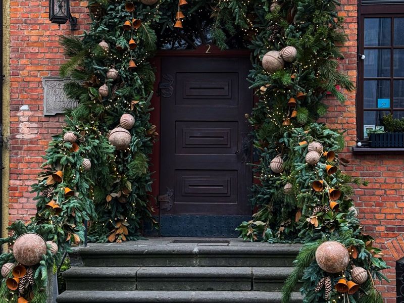 Brick townhouse entry framed in full fresh garland with magnolia, oversized ornaments and lanterns above stone steps