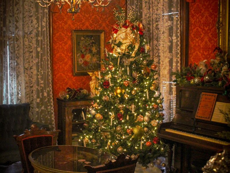 Victorian mansion parlor with a lit Christmas tree, crystal chandelier, red damask walls and a grand piano